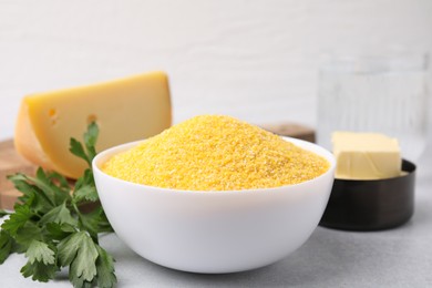 Raw cornmeal in bowl, parsley, cheese and butter on light table, closeup