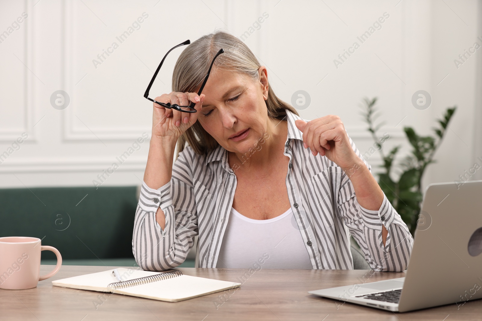 Photo of Menopause. Woman suffering from headache at wooden table indoors