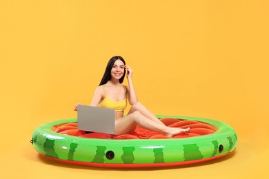 Happy young woman with beautiful suntan using laptop on inflatable mattress against orange background