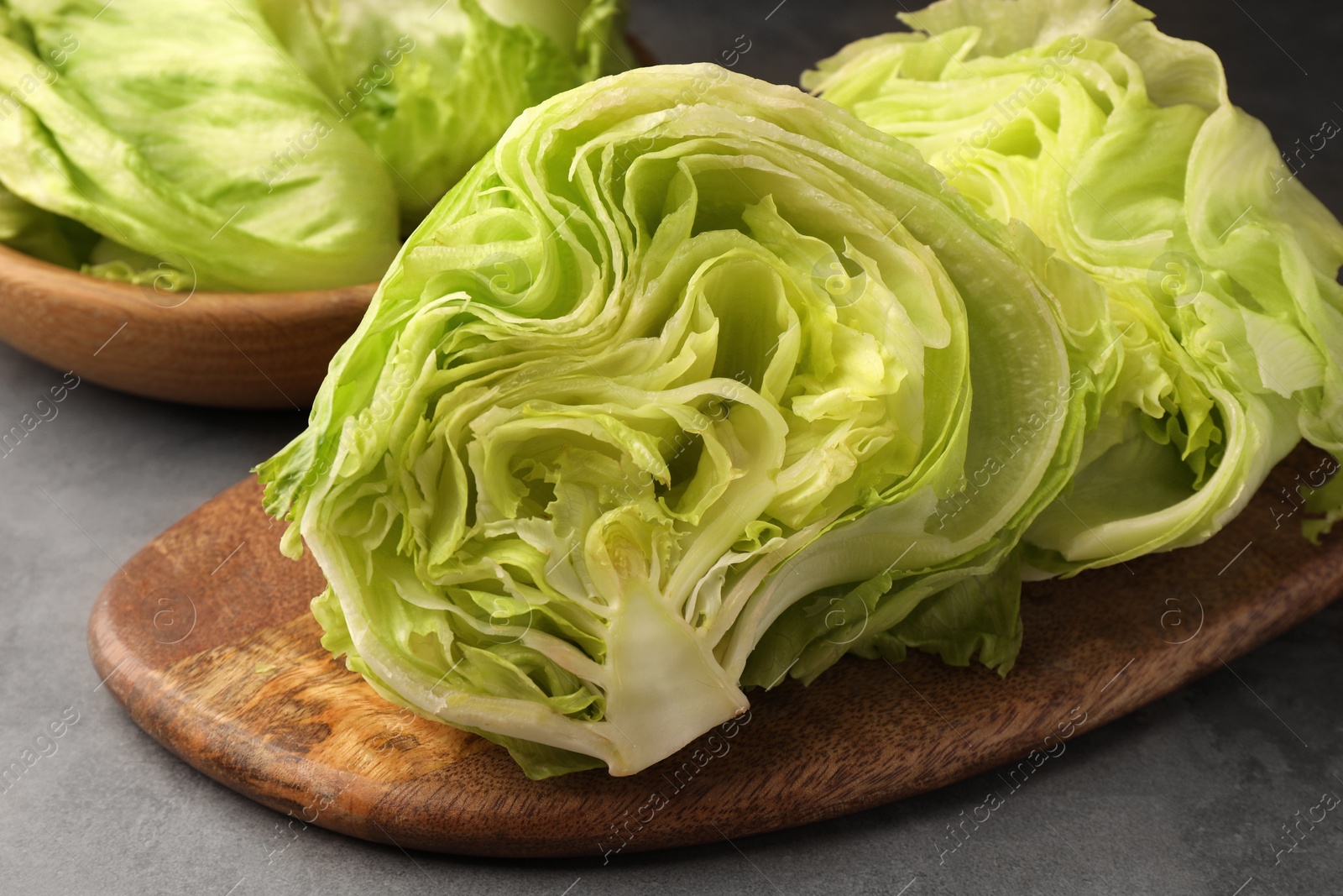 Photo of Board with halves of fresh green iceberg lettuce head on grey table, closeup
