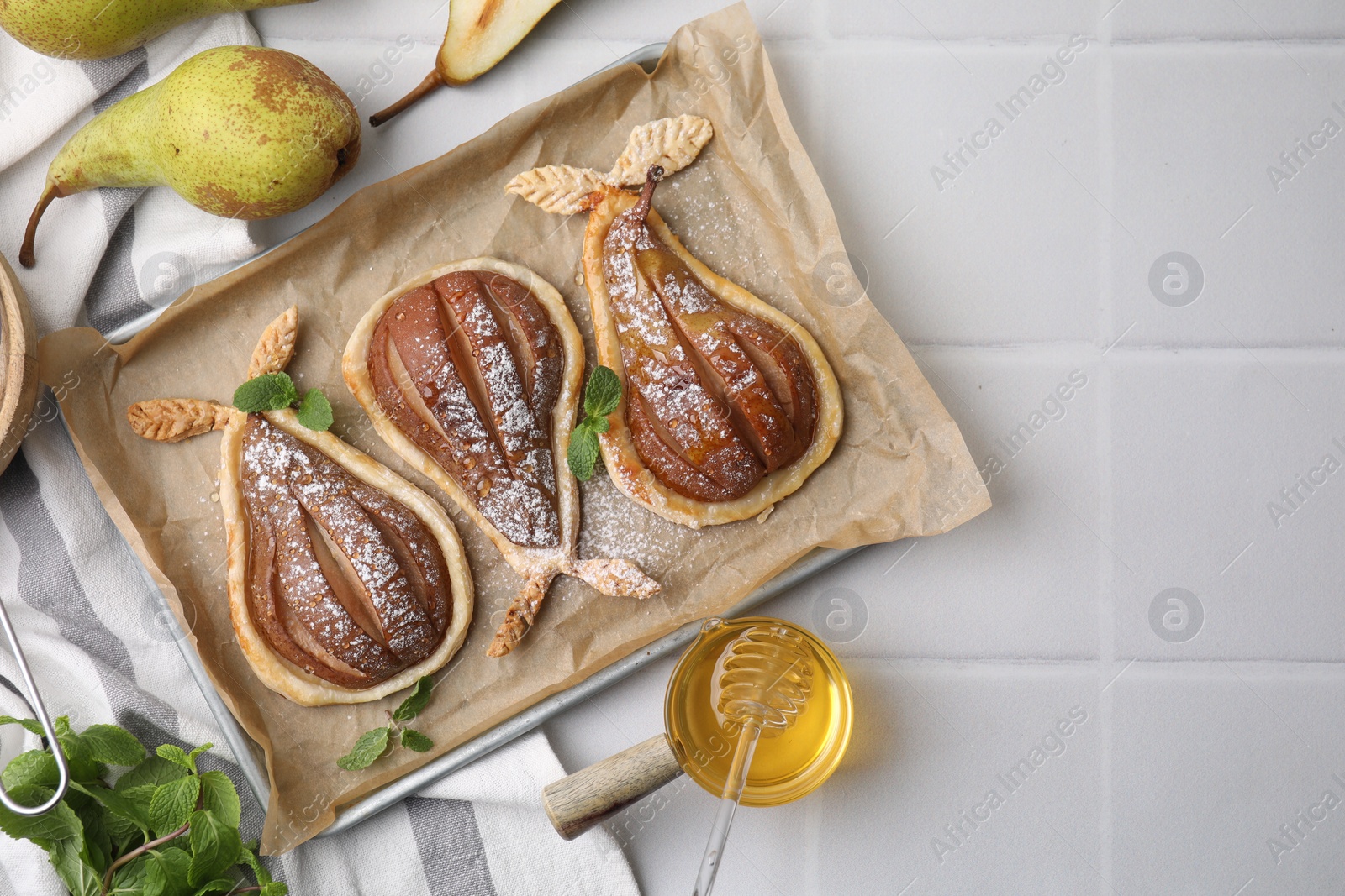 Photo of Delicious pears baked in puff pastry with powdered sugar served on white tiled table, flat lay. Space for text