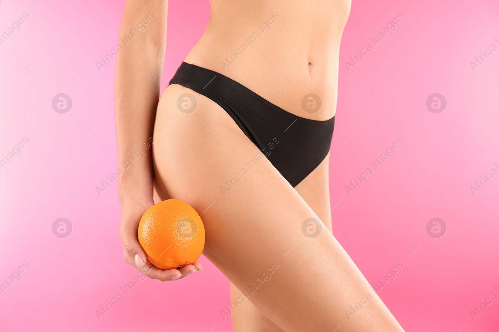 Photo of Closeup view of slim woman in underwear with orange on color background. Cellulite problem concept