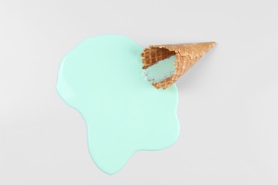 Melted ice cream and wafer cone on light blue background, top view