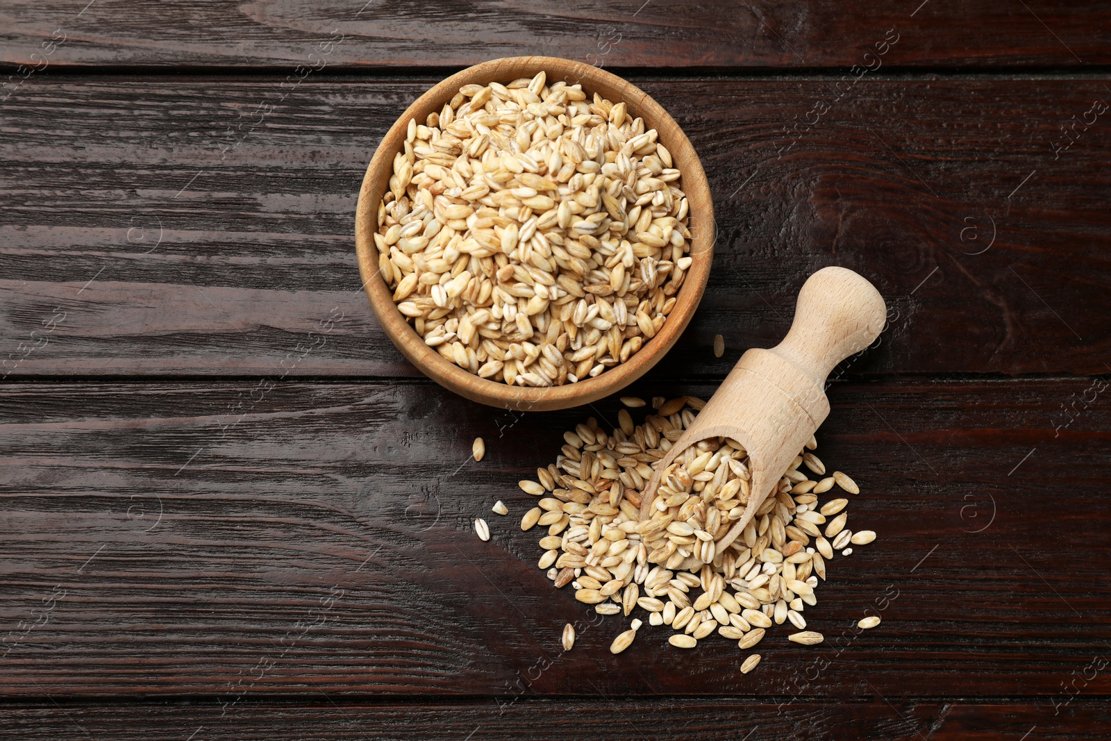 Photo of Dry pearl barley in bowl and scoop on wooden table, flat lay. Space for text