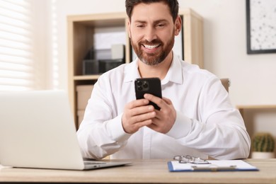 Photo of Smiling man using smartphone at table in office