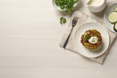 Delicious zucchini fritters with sour cream served on white wooden table, flat lay. Space for text