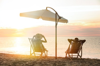 Photo of Couple relaxing on deck chairs at sandy beach. Summer vacation
