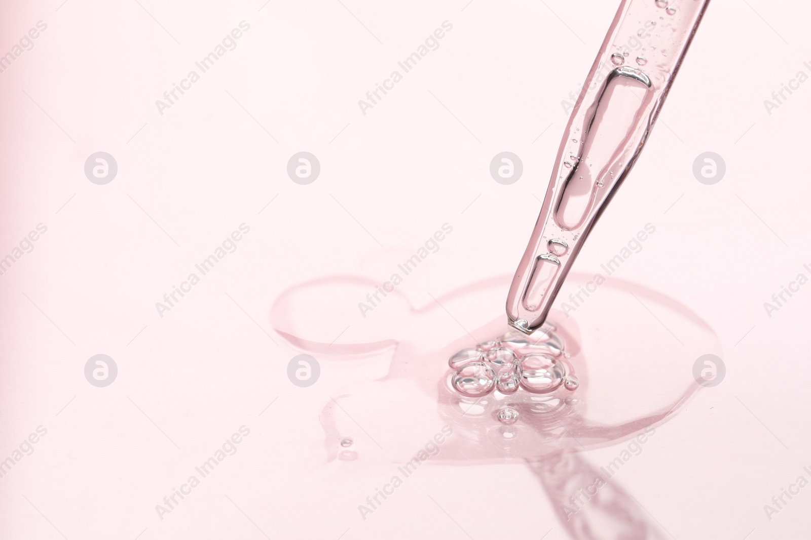 Photo of Glass pipette and transparent liquid on light pink background, closeup. Space for text