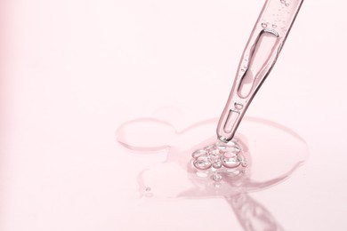 Photo of Glass pipette and transparent liquid on light pink background, closeup. Space for text