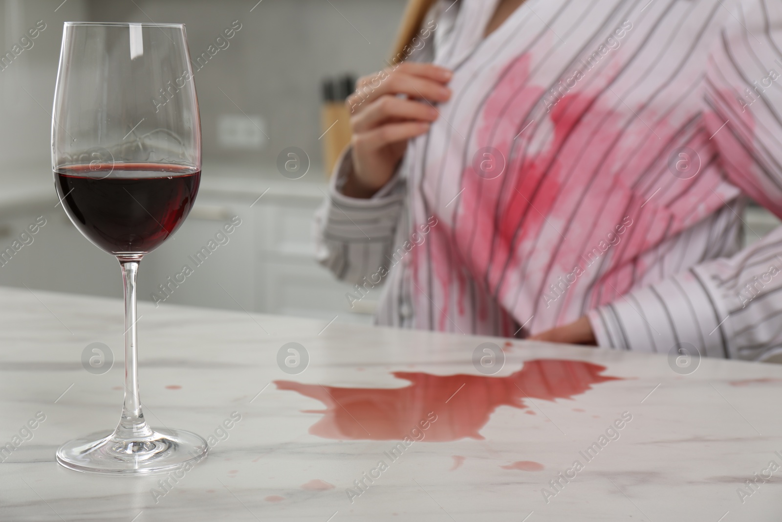 Photo of Woman with spilled wine over her shirt and marble table in kitchen, closeup