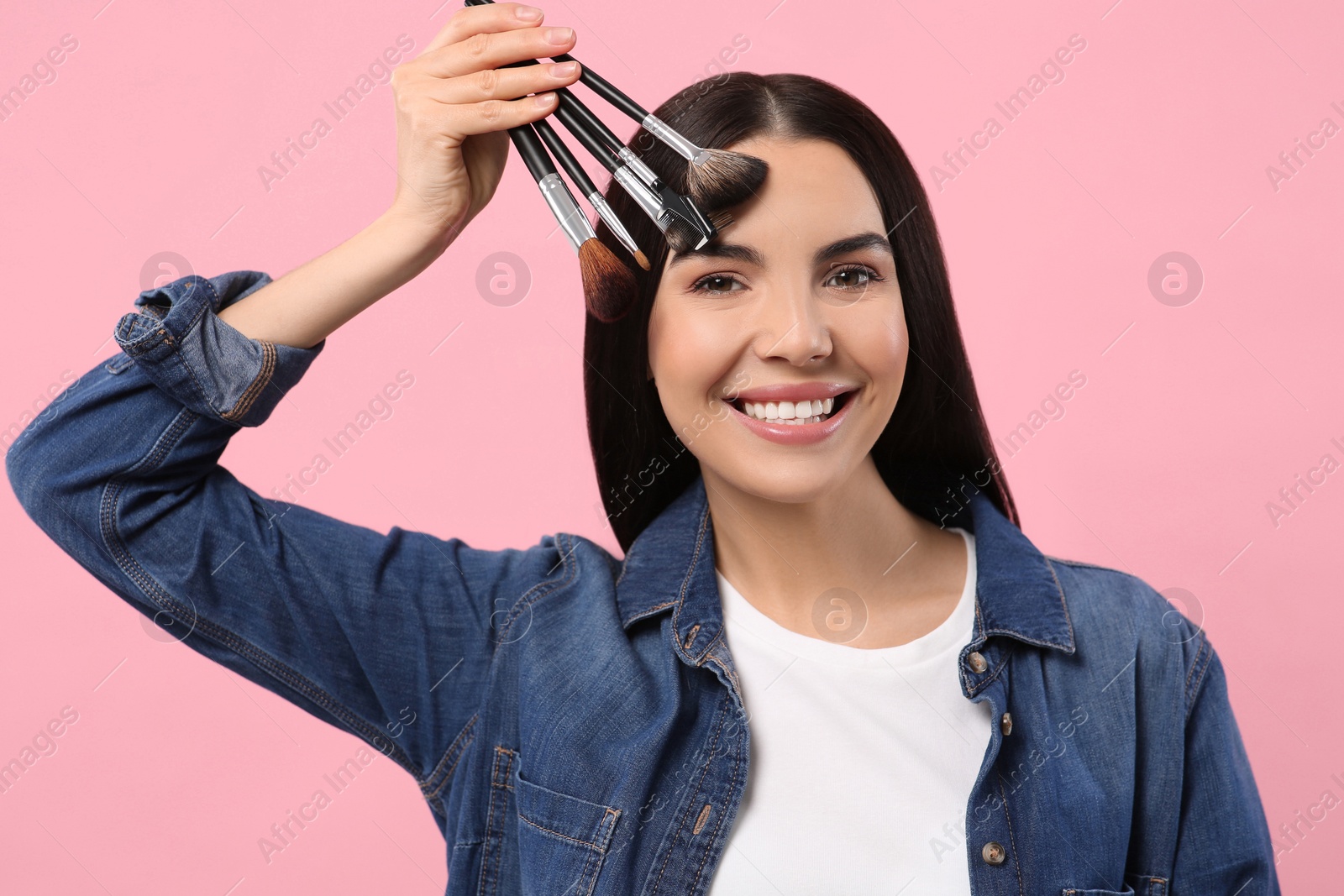 Photo of Happy woman with different makeup brushes on pink background