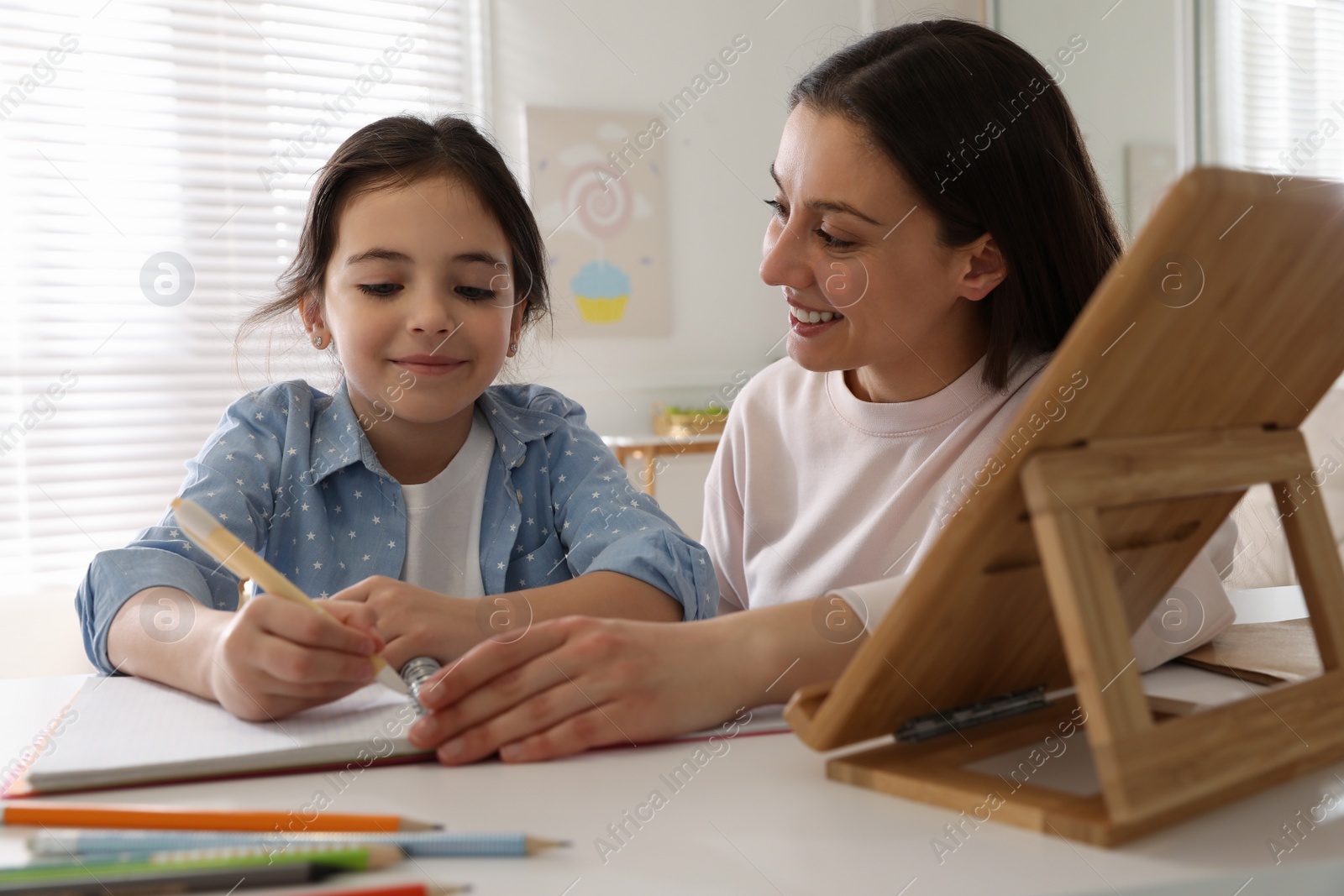 Photo of Mother helping her daughter with homework using tablet at home