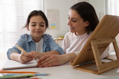 Photo of Mother helping her daughter with homework using tablet at home