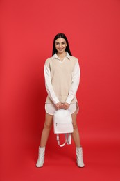 Photo of Young woman with stylish backpack on red background