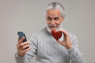 Photo of Happy senior man with smartphone showing red decorative heart on light grey background