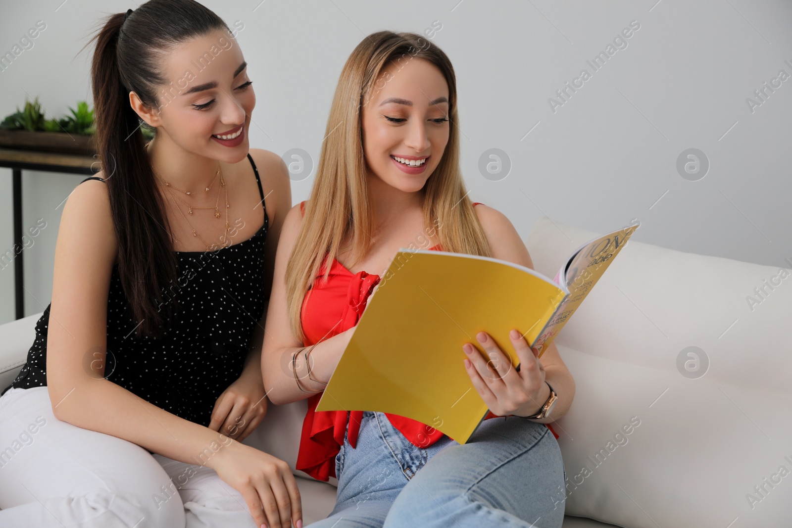 Photo of Happy women reading magazine on sofa indoors