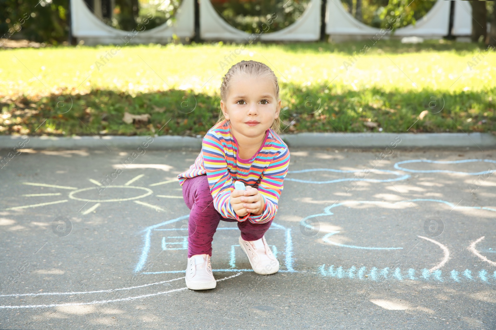 Photo of Little child drawing with colorful chalk on asphalt