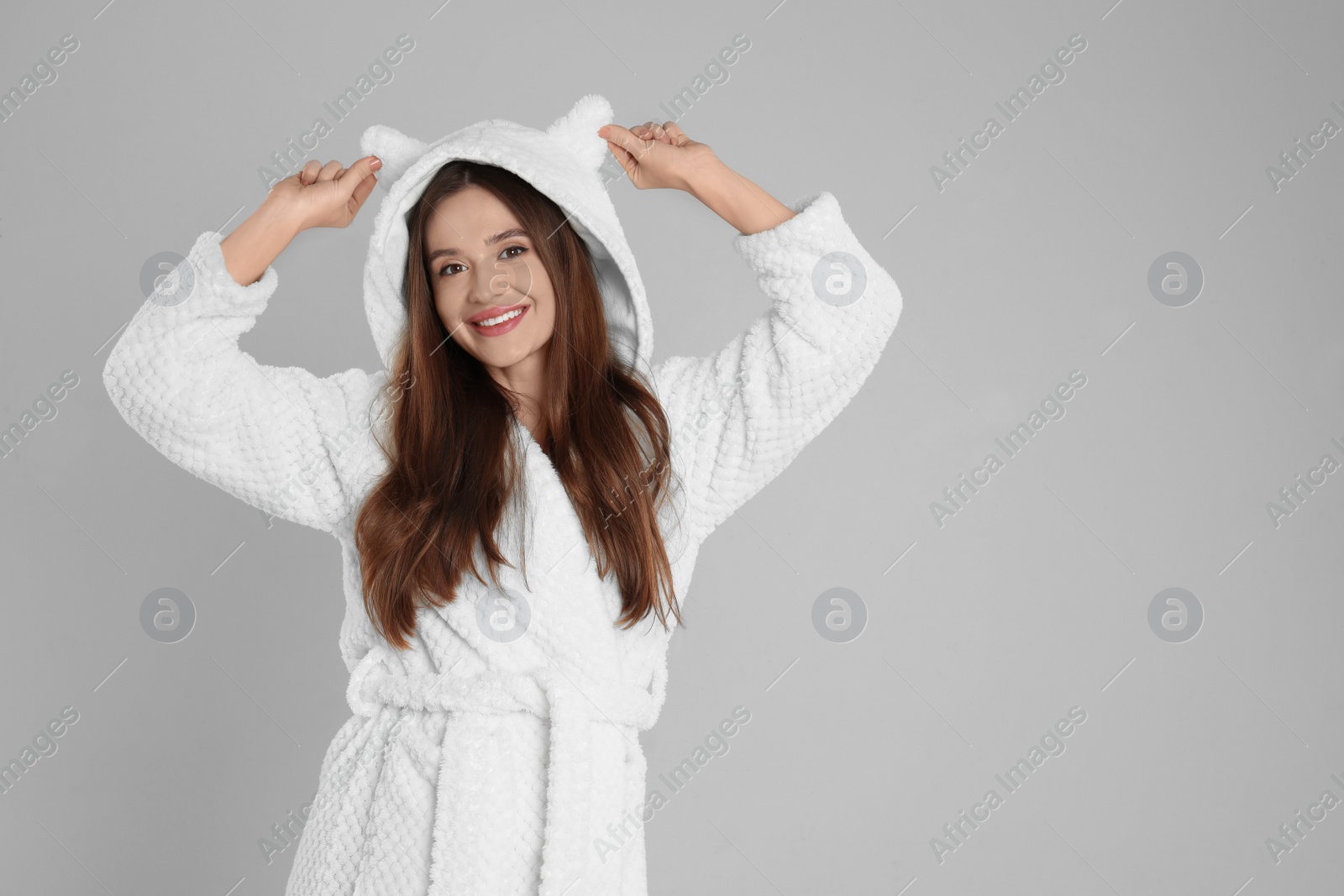 Photo of Beautiful young woman in bathrobe with funny hood on light grey background