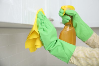 Photo of Woman cleaning white cupboard with rag and detergent indoors, closeup