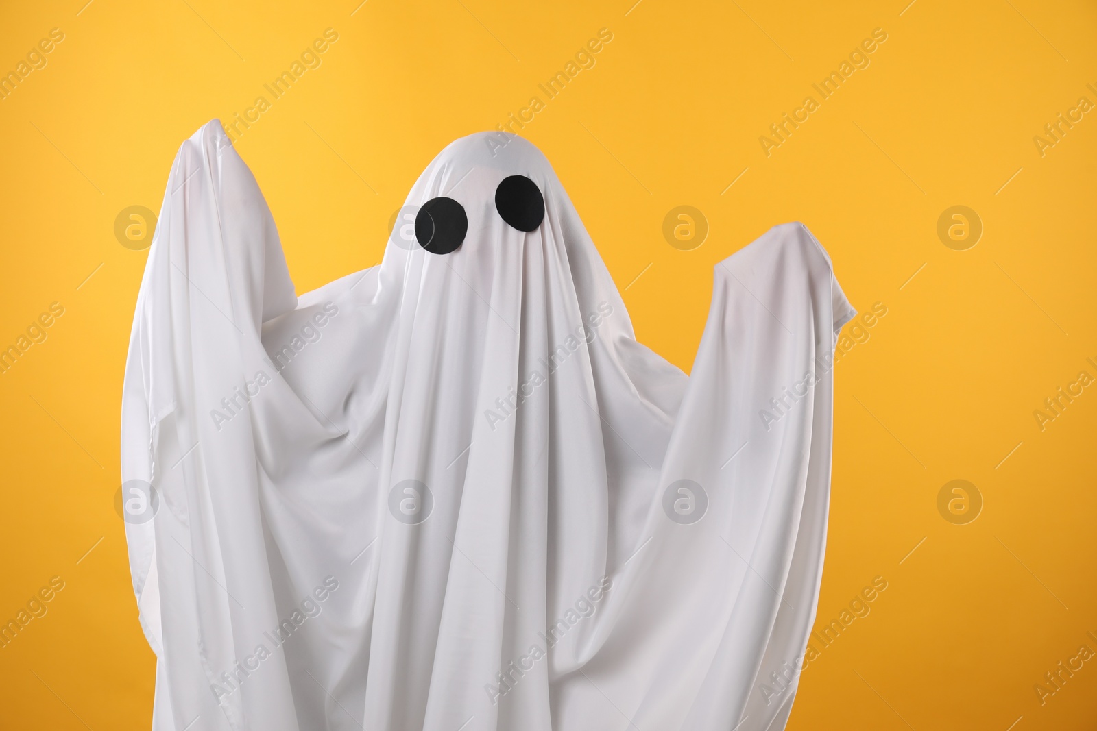 Photo of Creepy ghost. Person covered with white sheet on yellow background