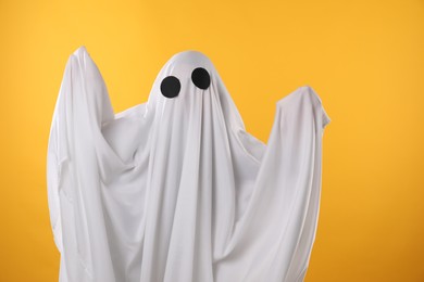 Photo of Creepy ghost. Person covered with white sheet on yellow background