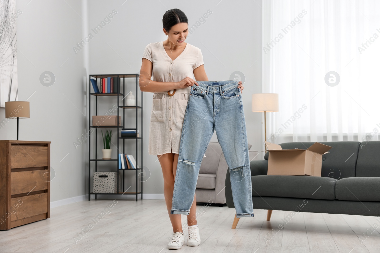 Photo of Young woman with just unpacked new jeans at home. Online shopping