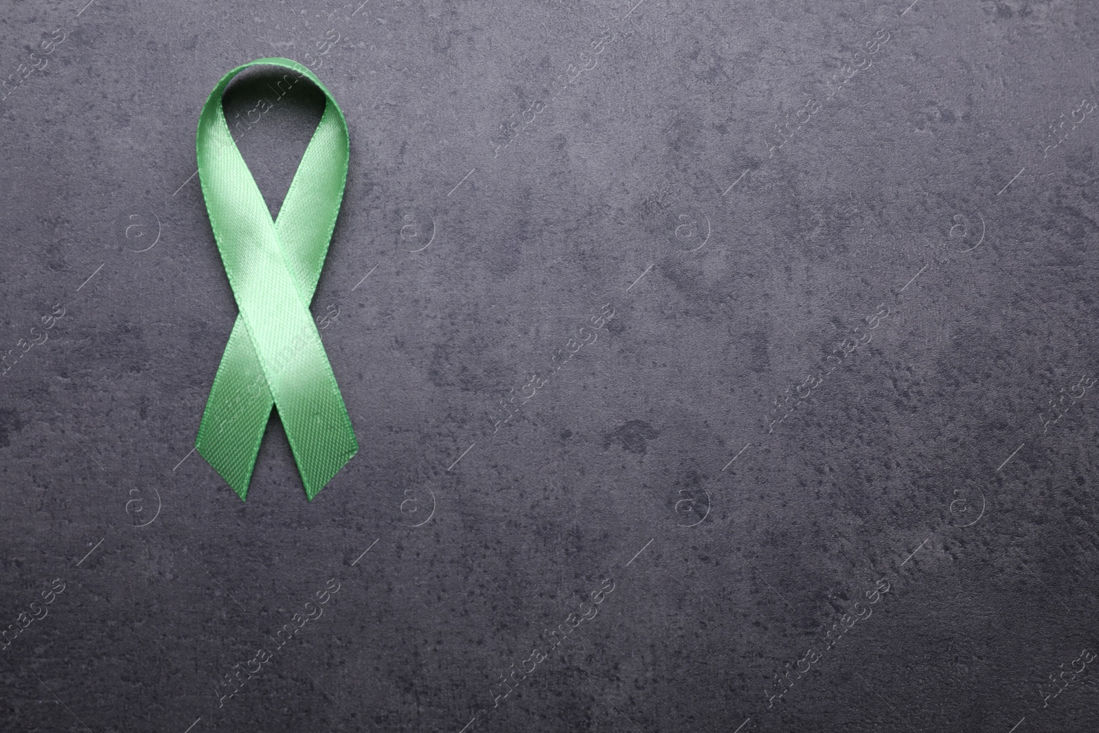 Photo of World Mental Health Day. Green ribbon on black background, top view with space for text