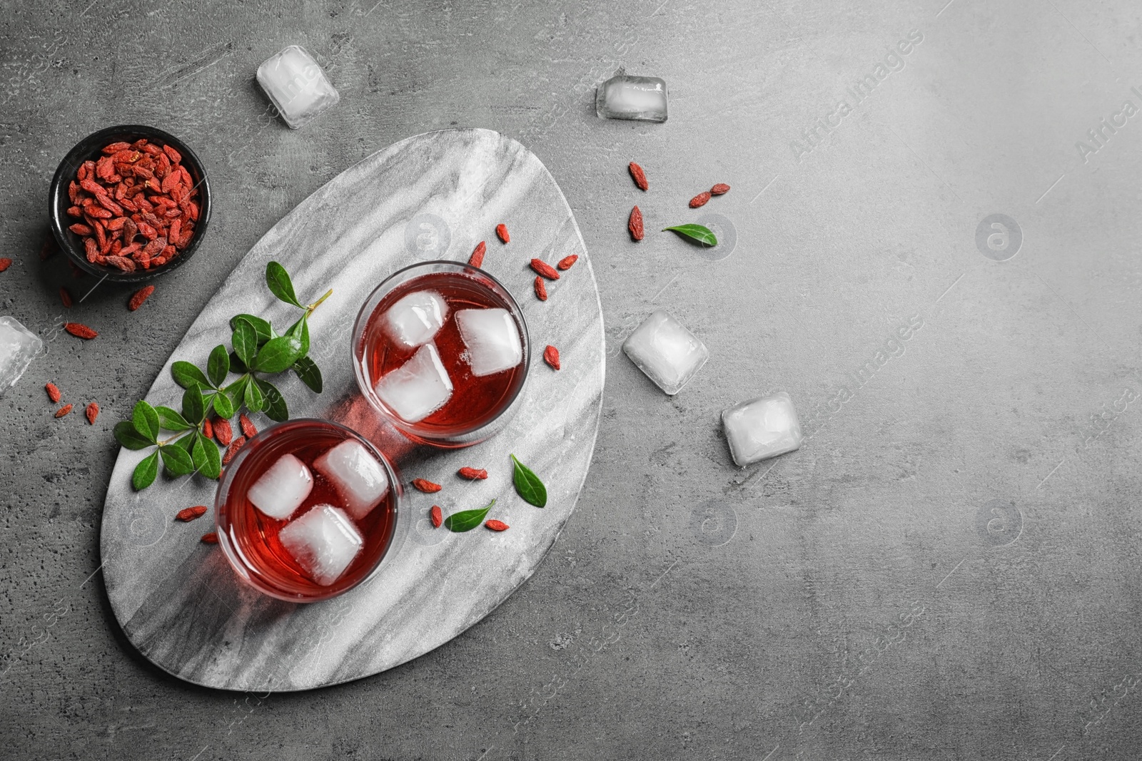 Photo of Healthy goji juice in glasses served on grey table, flat lay. Space for text