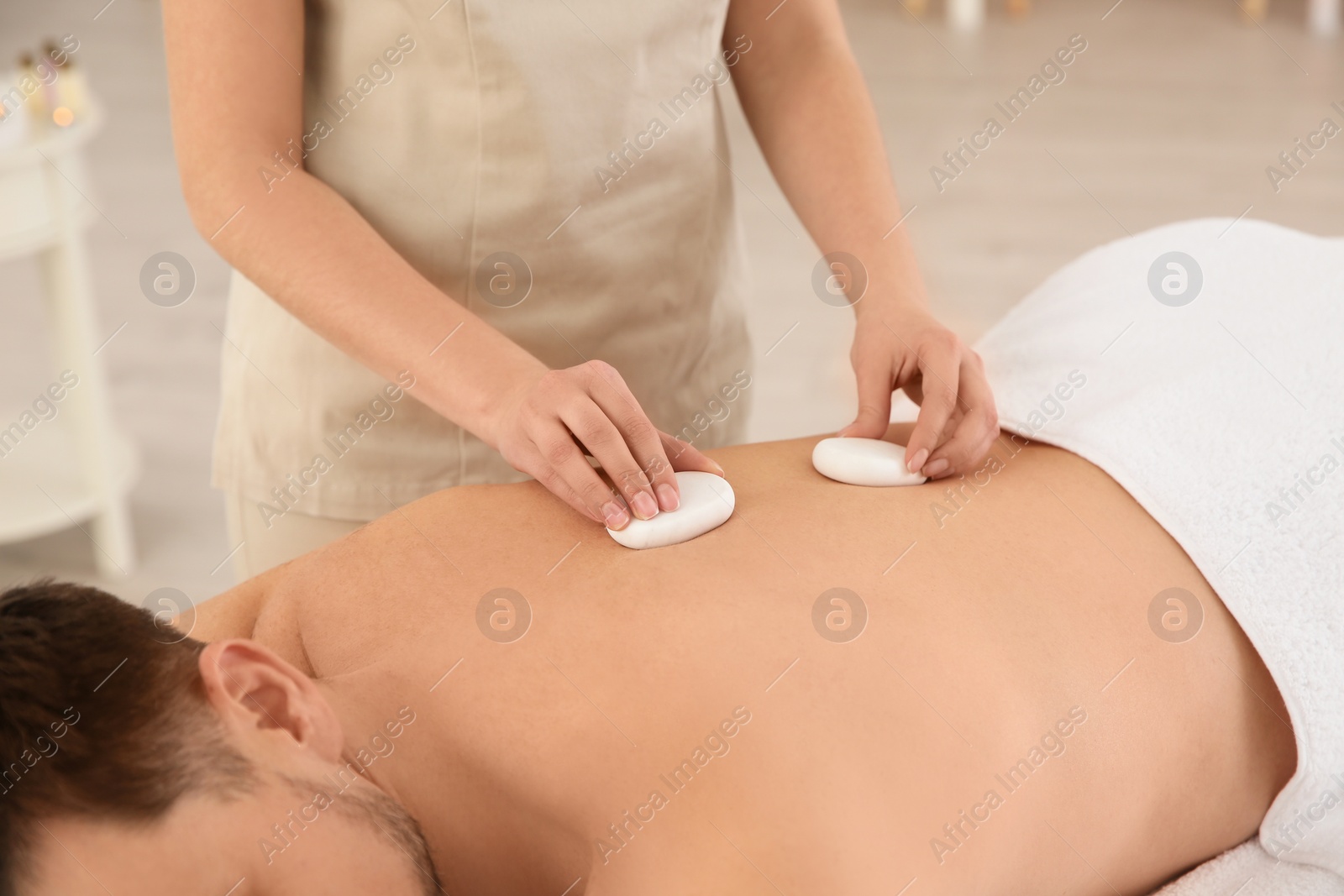 Photo of Man receiving hot stone massage in spa salon, closeup