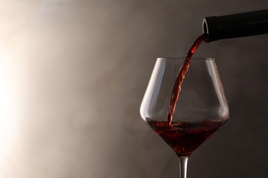 Photo of Pouring red wine from bottle into glass on color background. Space for text