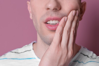 Young man with sensitive teeth on color background, closeup