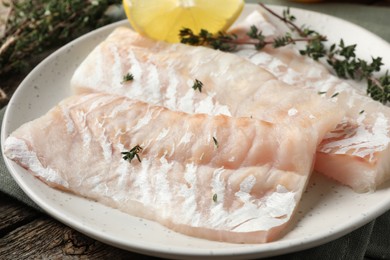 Photo of Fresh raw cod fillets with thyme and lemon on wooden table, closeup