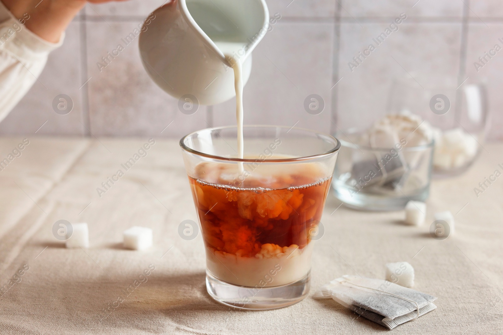 Photo of Pouring milk into cup with tea on light table, closeup