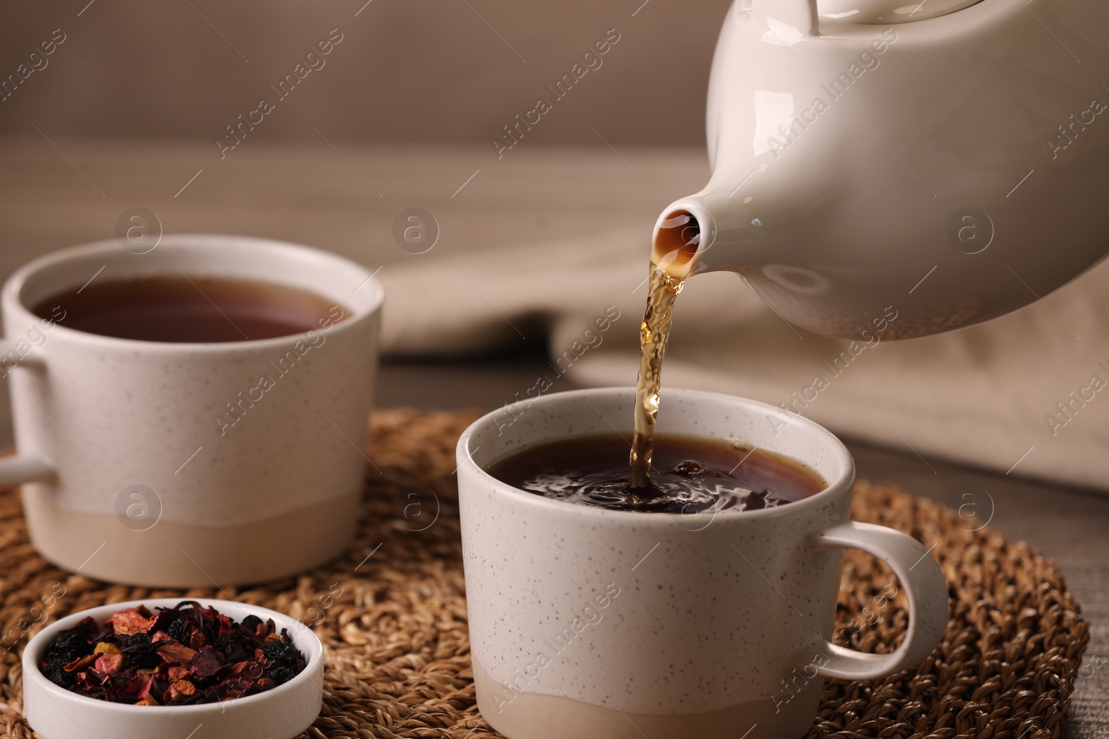 Photo of Pouring aromatic tea into cup at table, closeup