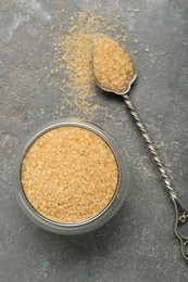 Photo of Brown sugar in bowl and spoon on grey textured table, top view