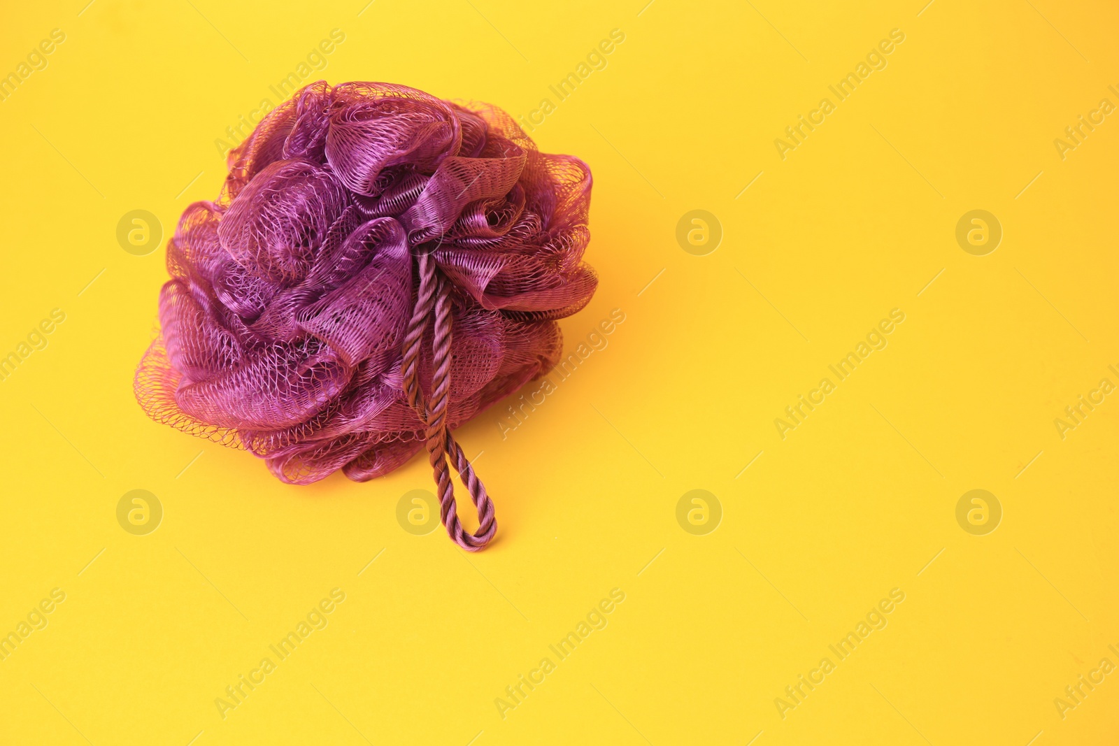 Photo of Purple shower puff on yellow background, space for text