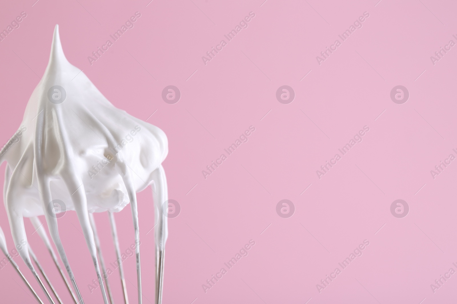 Photo of Whisk with whipped cream on pink background, closeup. Space for text