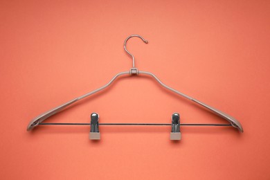 Photo of Empty hanger with clips on coral background, top view