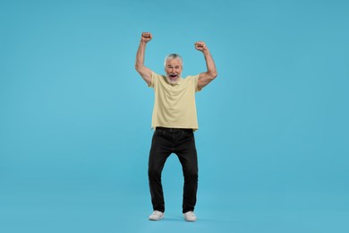 Photo of Emotional senior sports fan celebrating on light blue background