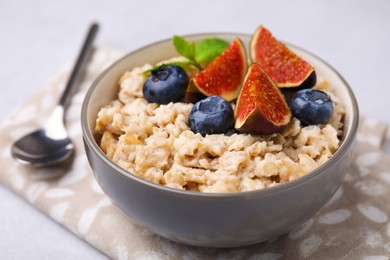 Oatmeal served with blueberries, mint and fig pieces on light grey table, closeup