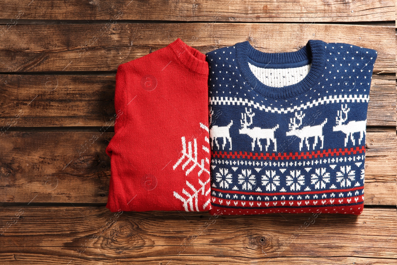 Photo of Christmas sweaters with pattern on wooden background, top view