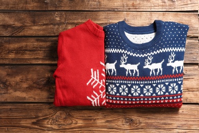 Christmas sweaters with pattern on wooden background, top view