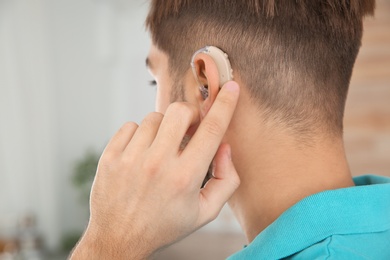 Young man adjusting hearing aid at home, closeup