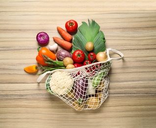 Fresh vegetables in eco mesh bag on wooden table, flat lay