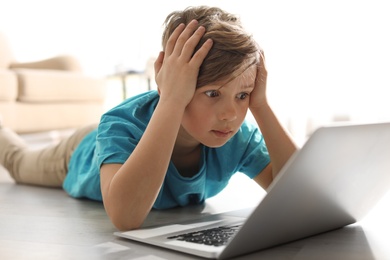 Photo of Shocked little child with laptop on floor indoors. Danger of internet