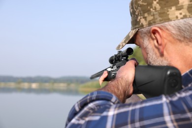 Photo of Man aiming with hunting rifle near lake outdoors, closeup. Space for text
