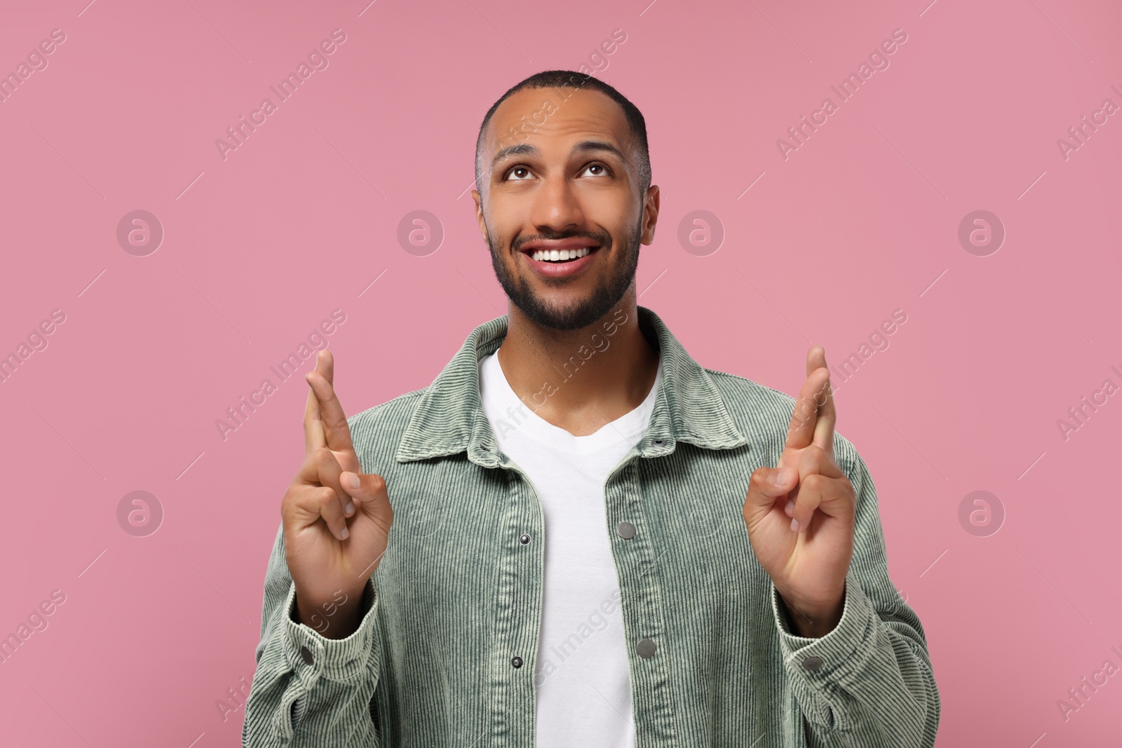 Photo of Happy man crossing his fingers on pink background