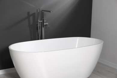 Photo of Stylish ceramic tub near grey wall in bathroom