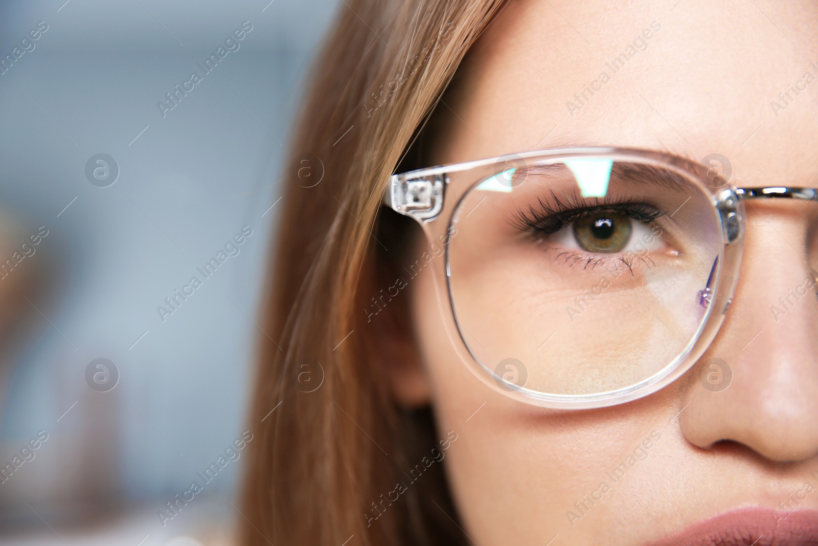 Photo of Young woman wearing glasses on blurred background, closeup. Ophthalmology service