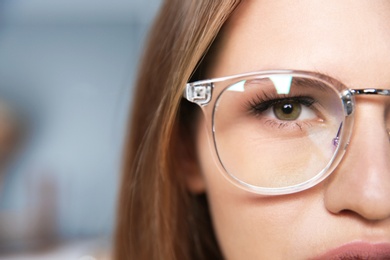 Photo of Young woman wearing glasses on blurred background, closeup. Ophthalmology service